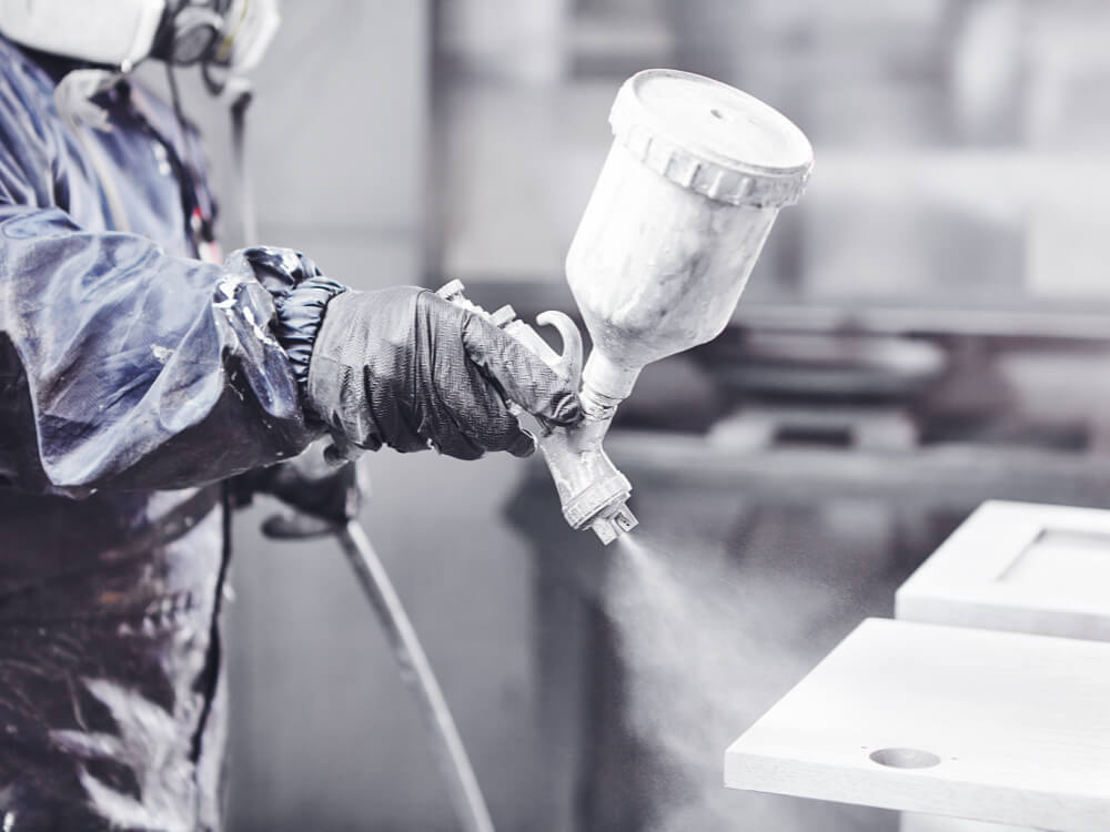 Industrial worker applying UV coating to wooden surface using spray gun