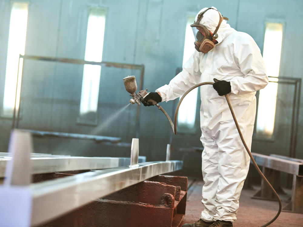 Worker in protective suit applying UV-resistant OEM coating to large metal structure