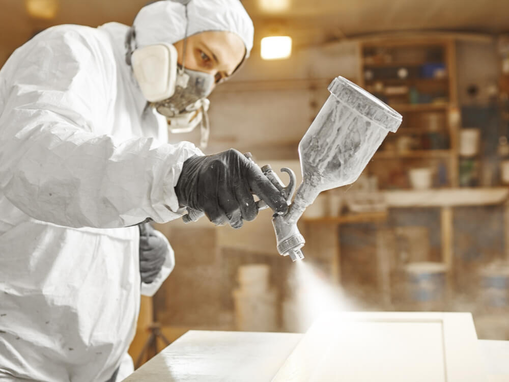 Worker spray painting cabinet panel in protective gear with UV-curable coating