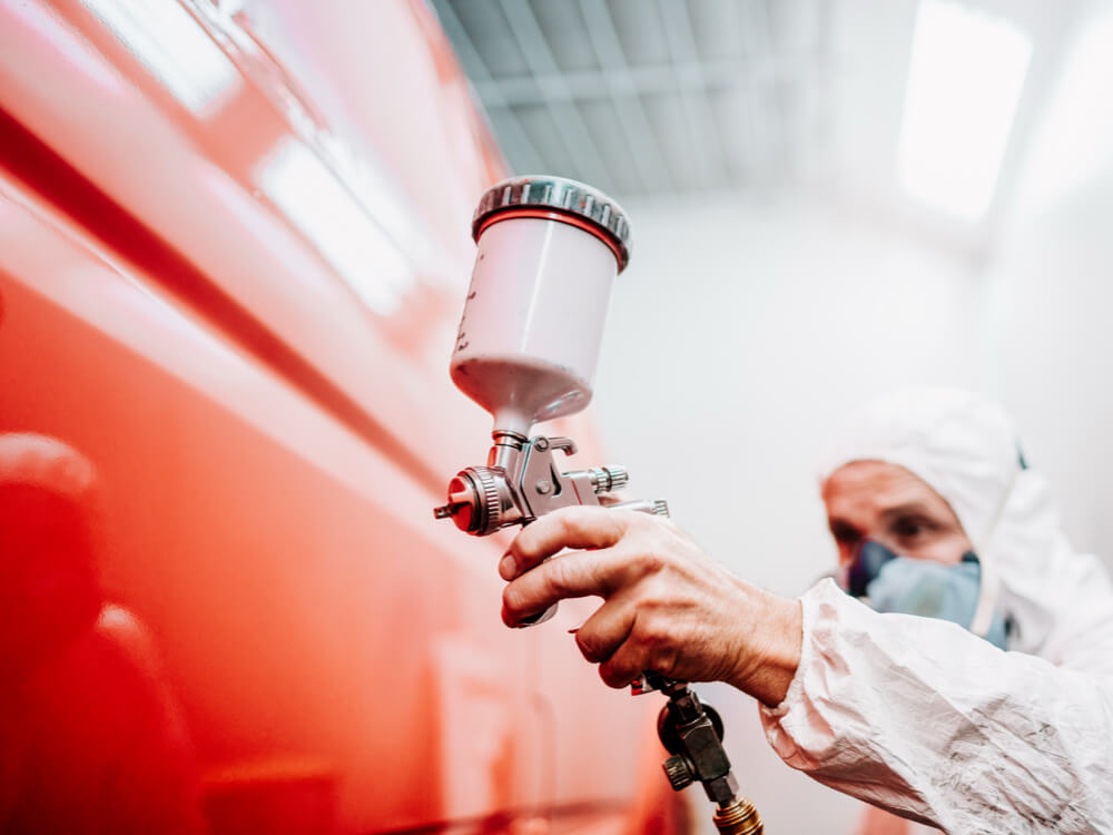 Technician spray painting red automotive surface with UV-resistant industrial coating